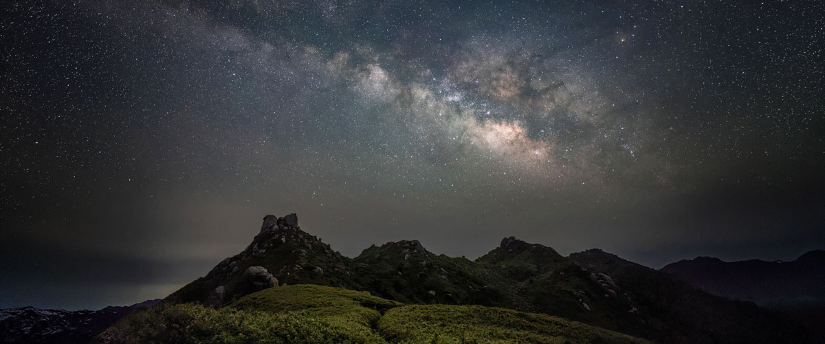 Milchstraße über einer dunklen Berglandschaft unter klarem Sternenhimmel
